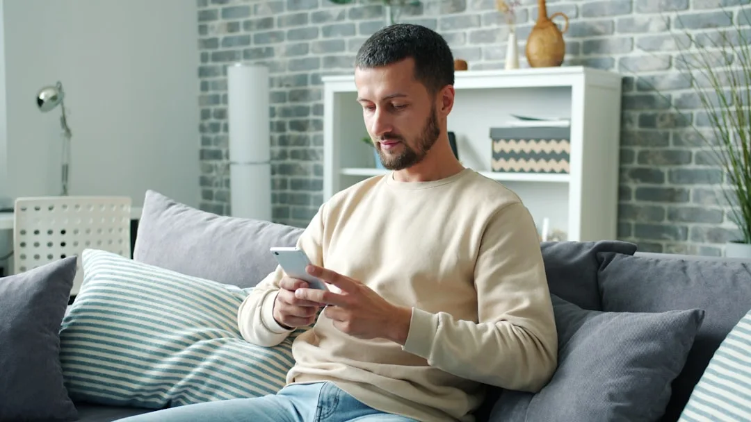 A person sitting comfortably at home, thoughtfully typing a polite reply to an invitation on their phone