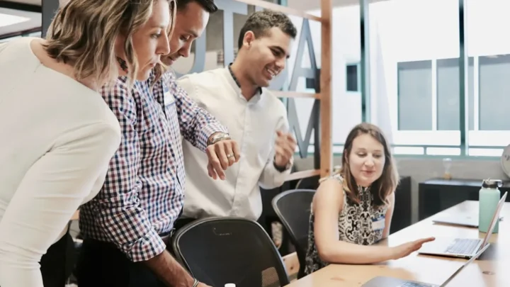 Two colleagues smiling in a bright office as one accepts a compliment from the other