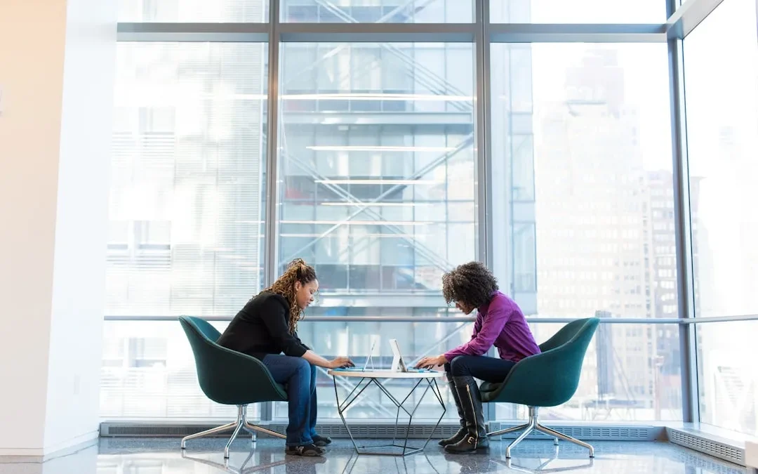 Two coworkers in a quietly tense conversation across a desk in an office