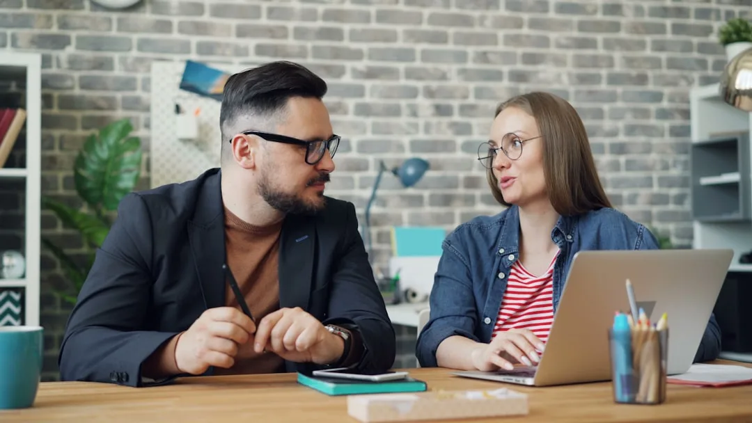 Two coworkers at a desk having a calm, constructive feedback conversation