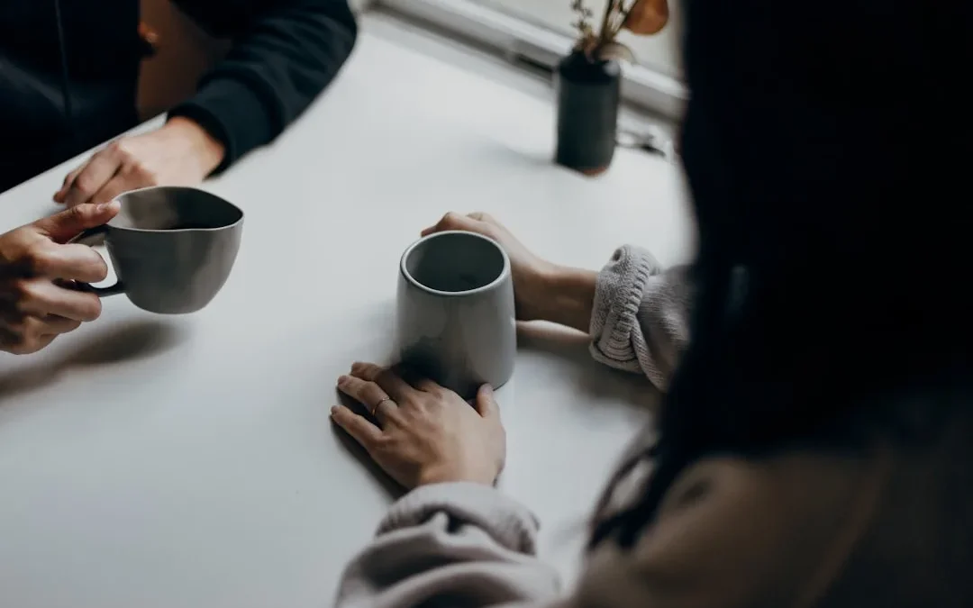 Two friends chatting warmly over coffee, one genuinely asking how the other is doing