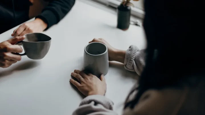 Two friends chatting warmly over coffee, one genuinely asking how the other is doing