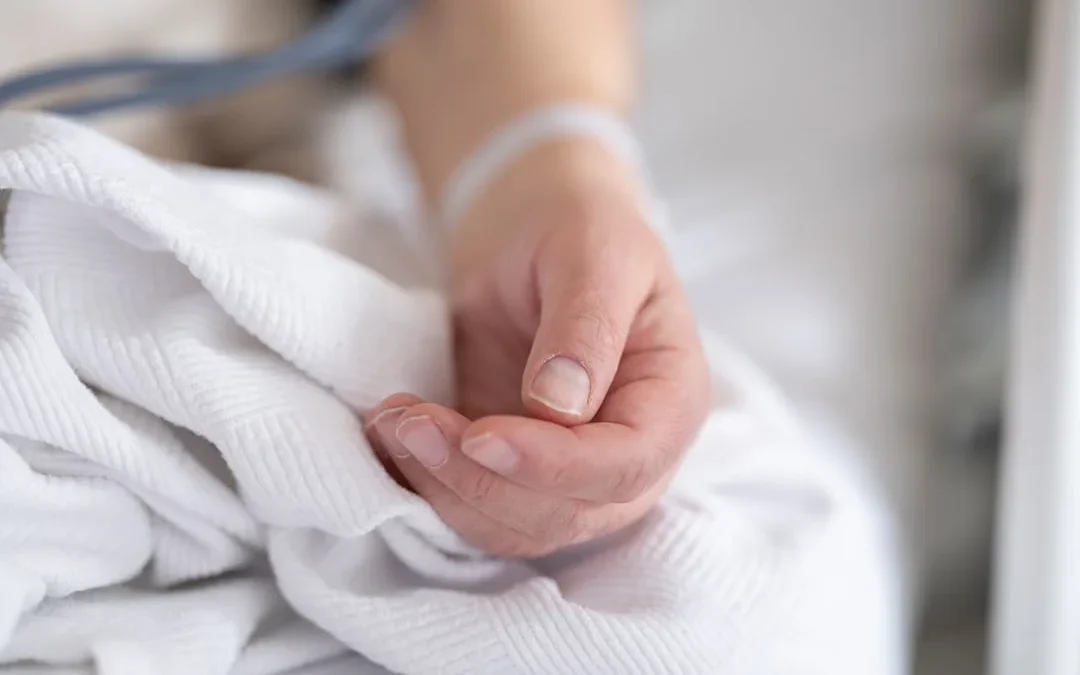 Two hands gently held together, offering quiet comfort at a bedside