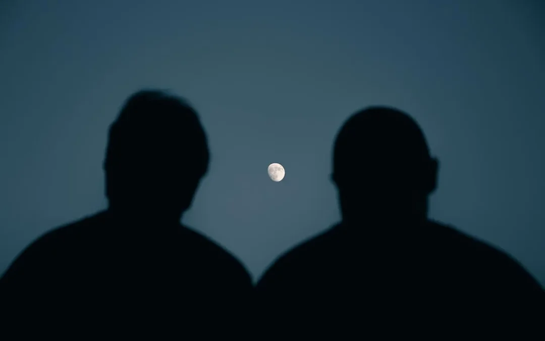 two people quietly watching a bright moon together at night
