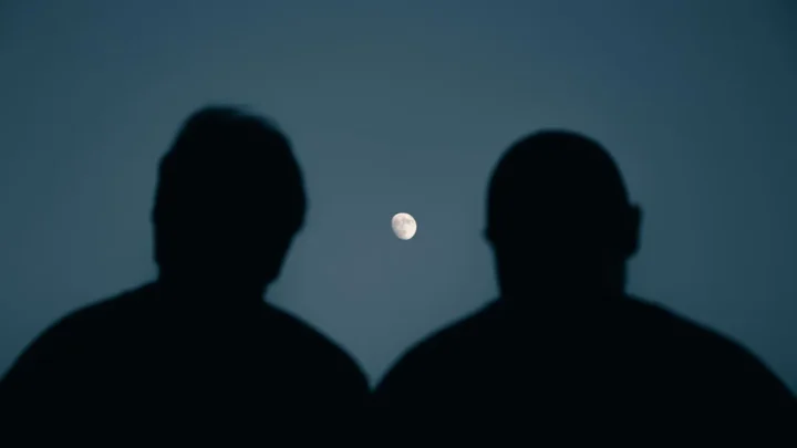 two people quietly watching a bright moon together at night