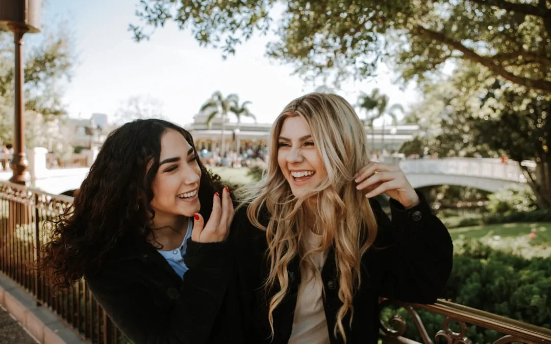 2 women smiling and standing near trees during daytime