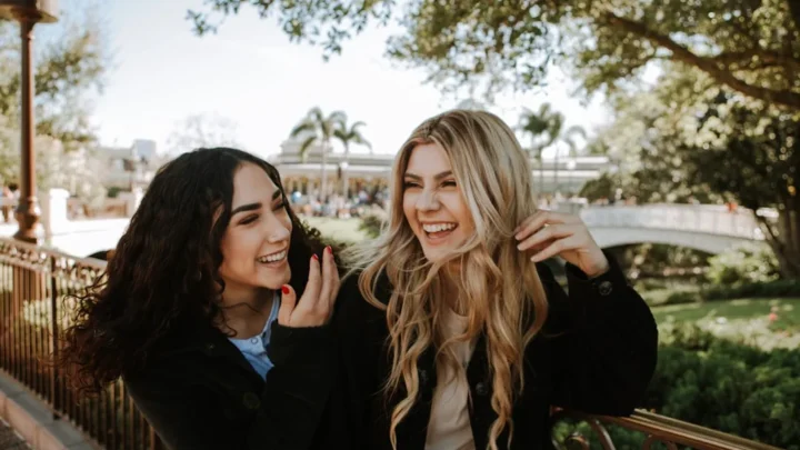 2 women smiling and standing near trees during daytime