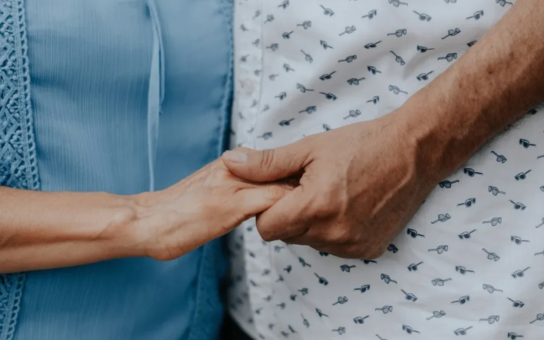 Two people holding hands, one wearing a blue shirt and one a patterned shirt