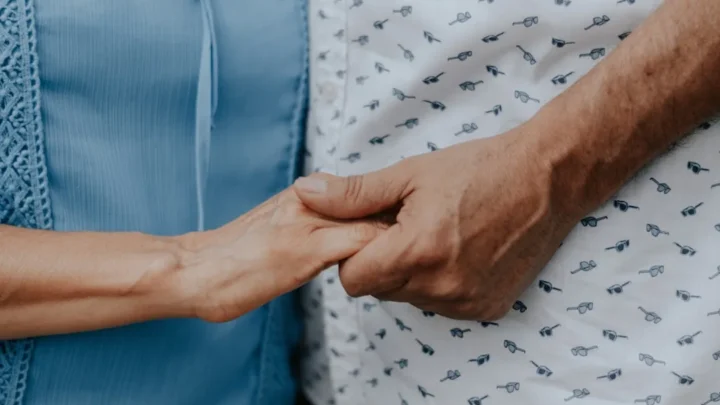 Two people holding hands, one wearing a blue shirt and one a patterned shirt